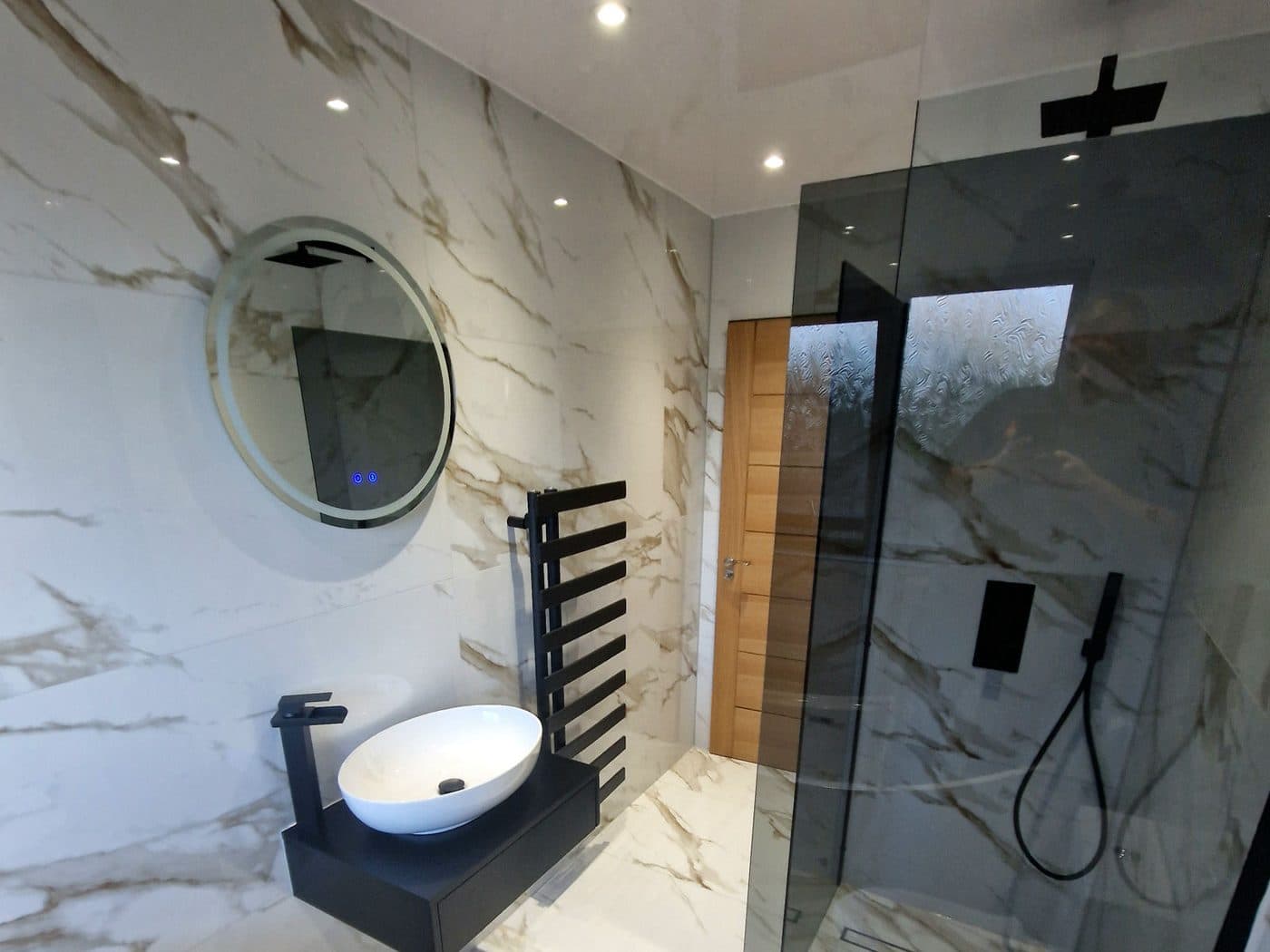 A finished bathroom in book-matched marble-effect porcelain with a black basin and walk-in shower