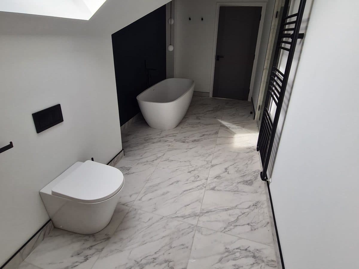 A freestanding bath under a skylight in a loft bathroom, large-format marble-effect floor tiles