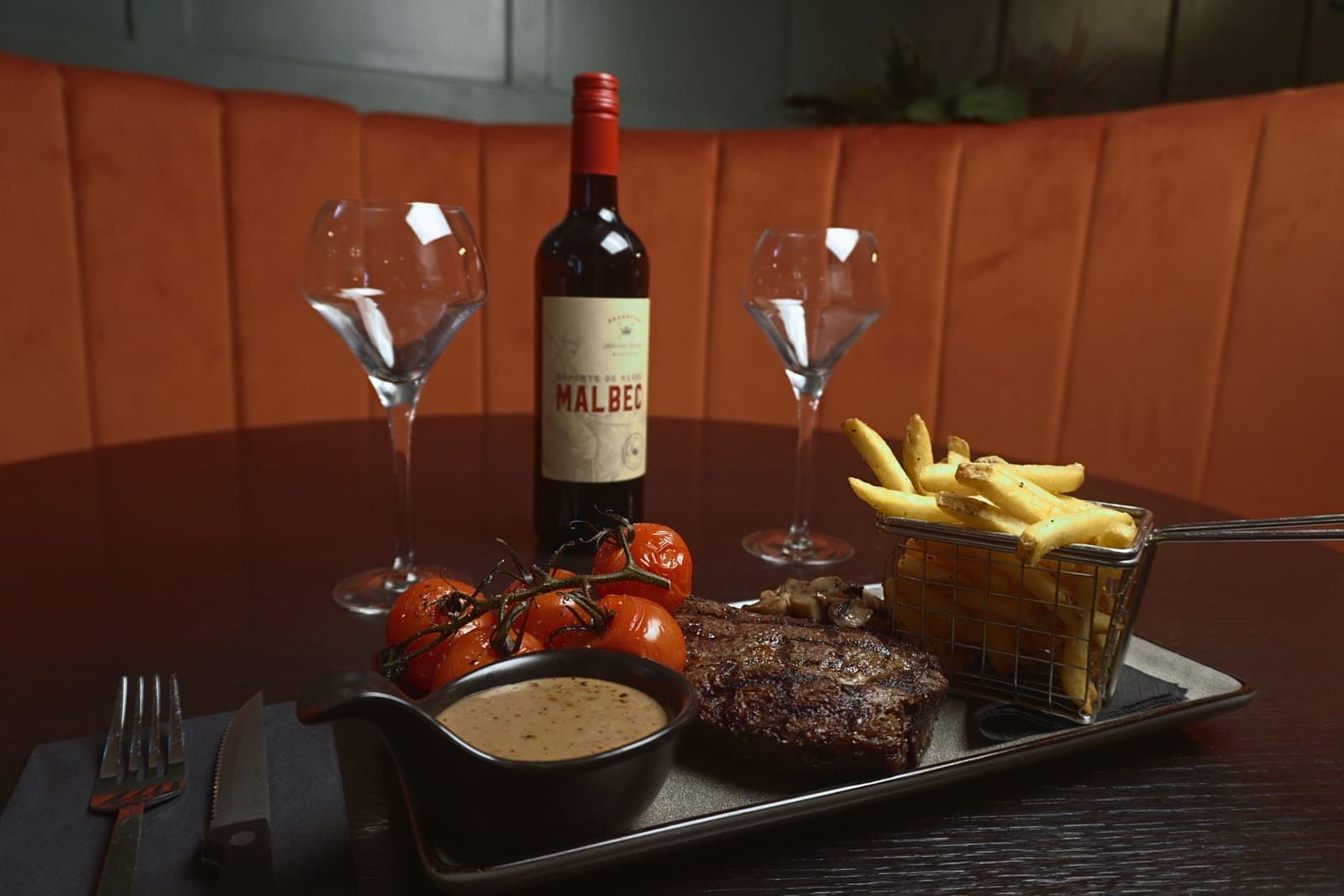 The finished photo: a steak, tomatoes and fries on a slate, with a bottle of Malbec in the orange booth