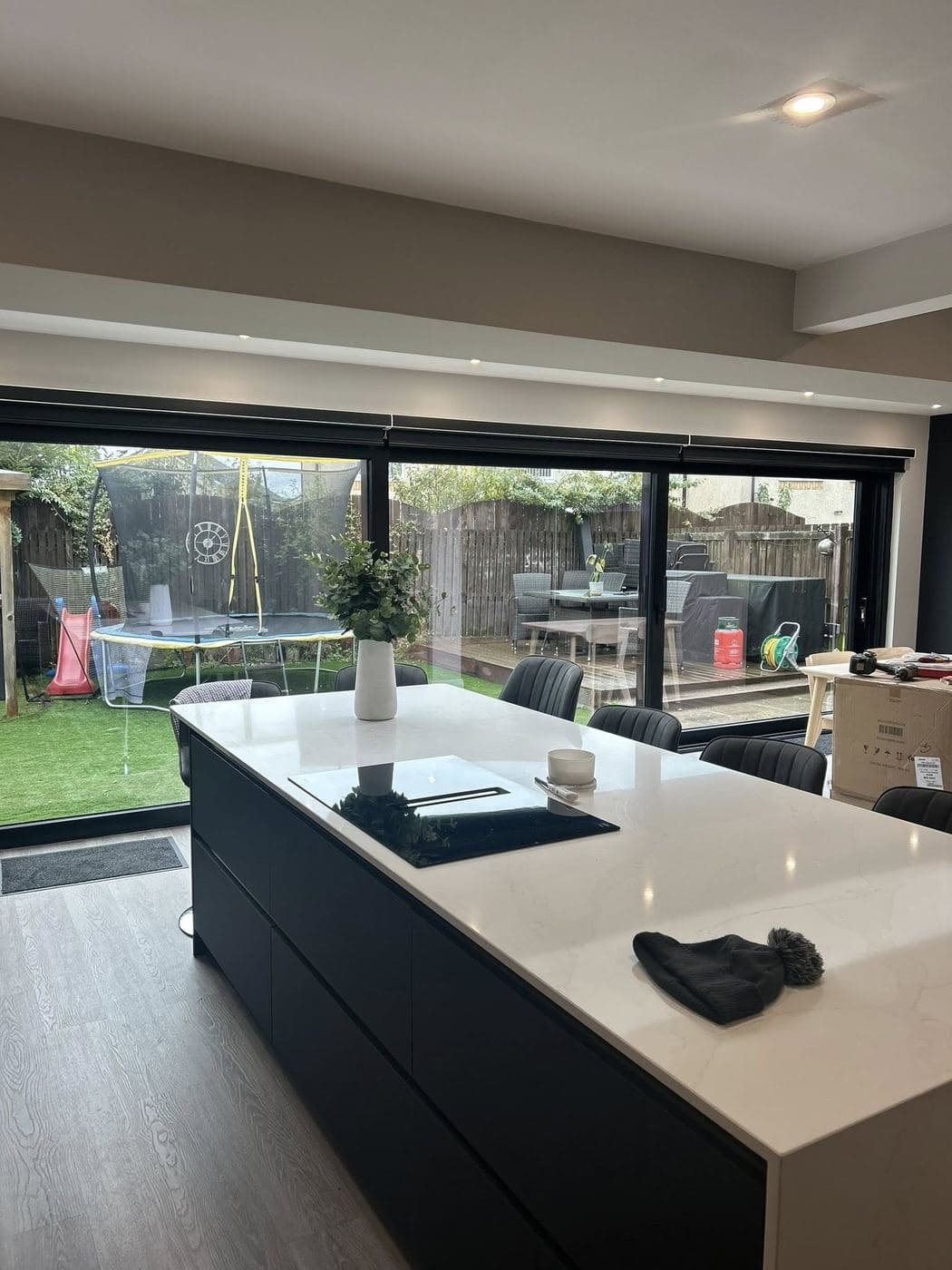 A finished kitchen with a dark island, quartz worktop and full-width glazing onto a garden