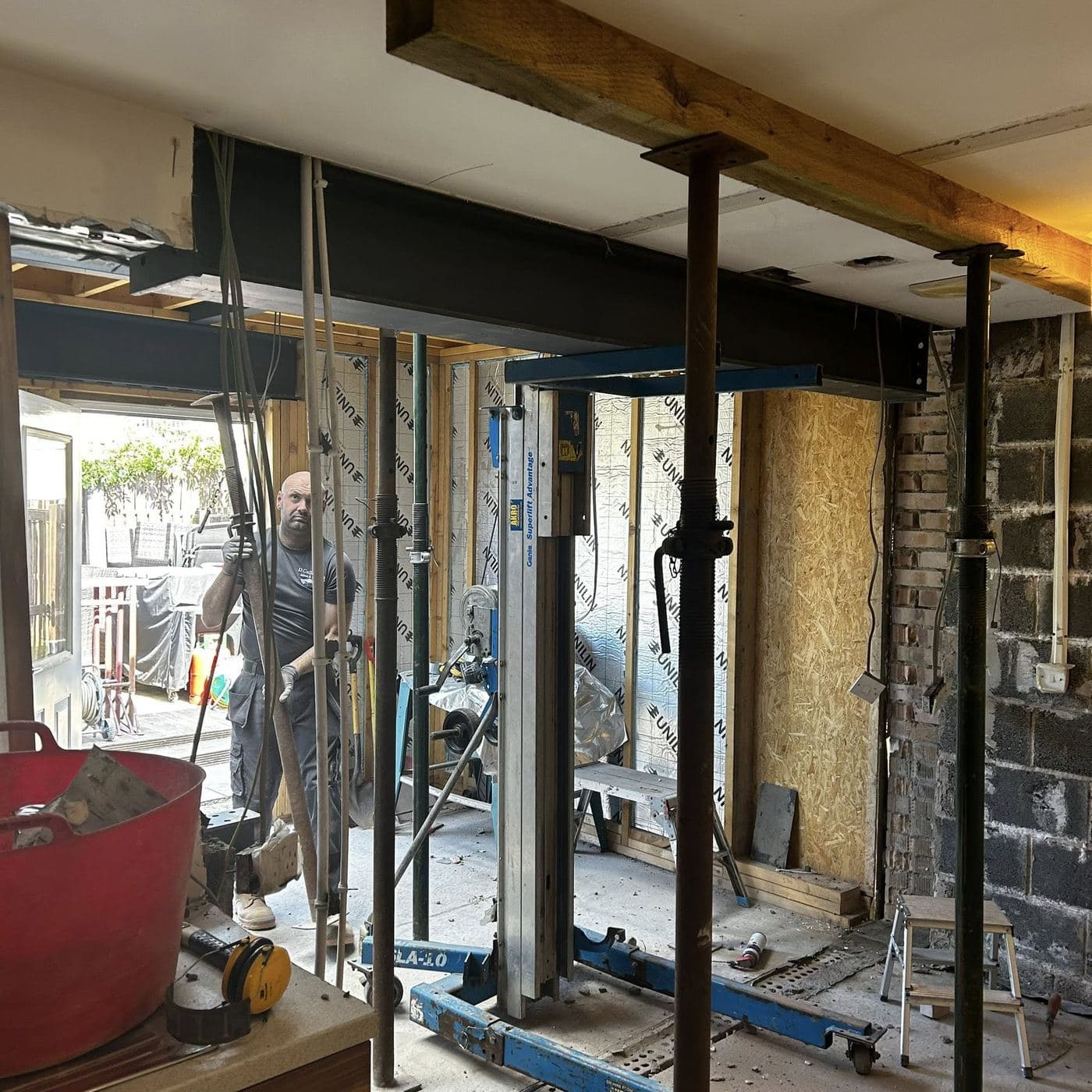A D. Callaghan joiner steadying an acrow prop under a newly fitted steel beam
